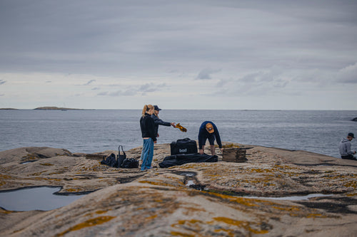 Personer packar upp bastutältsutrustning på klippor vid havet.