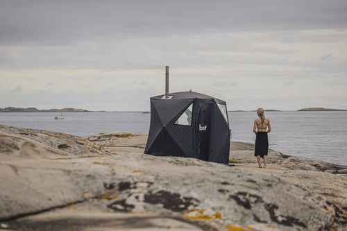Svart bastutält från bast på klippor vid havet med ånga ur skorstenen